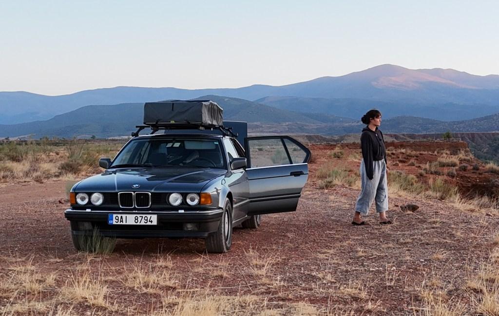 Woman standing next to a classic BMW with rooftop tent in Andalusia